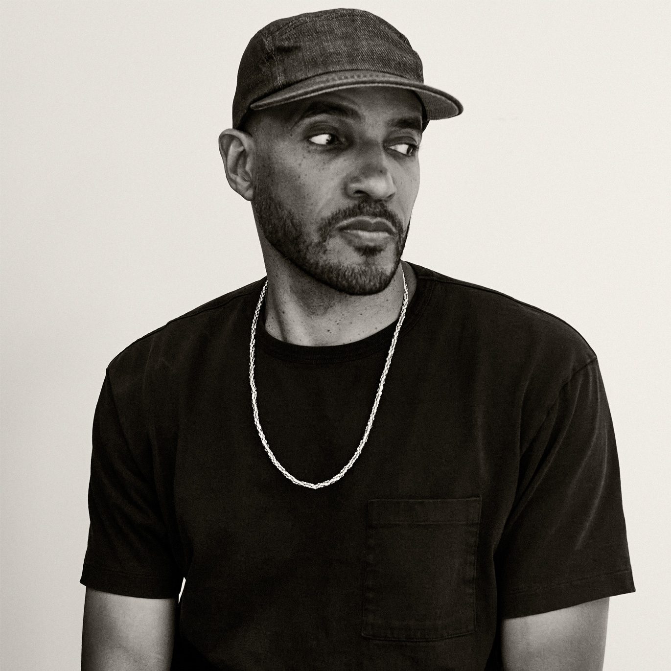 A black and white photo of a Black man wearing a black t-shirt and a gold chain